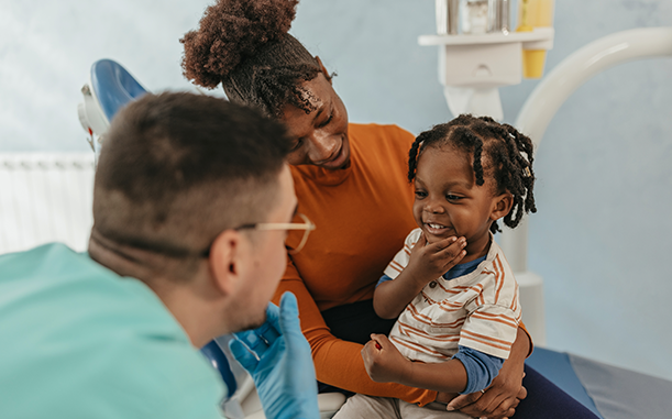 A parent and young child, representing a Black ALICE household, sit in a dentist’s chair – with the child on the parent’s lap, talking to the dentist.