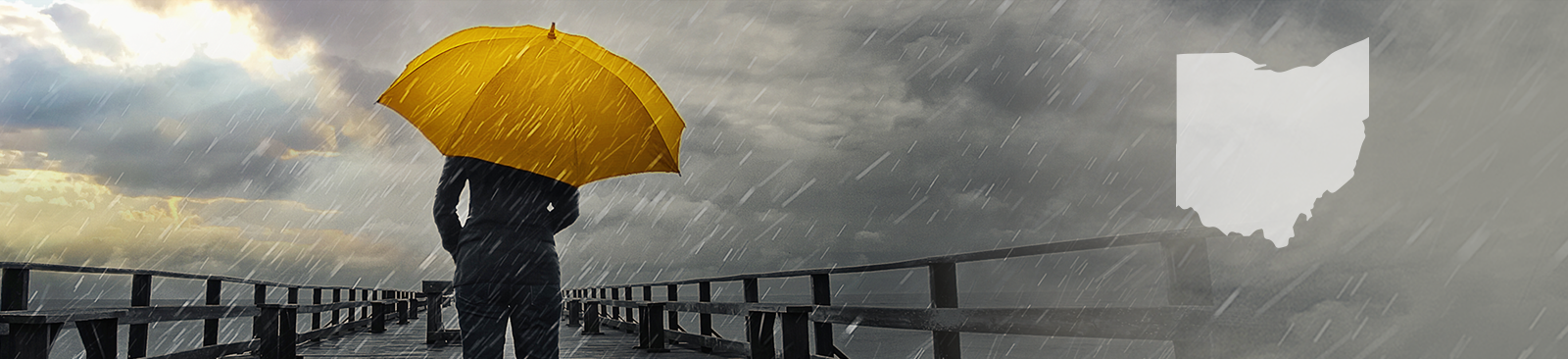A person stands with their back to the camera, carrying a bright yellow umbrella in the middle of a storm. They stand on a pier, looking out at the stormy sky, which simultaneously looks threatening and hopeful as some of the clouds part to reveal a glimpse of sunshine.