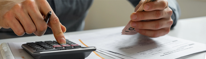 Close up of a person's hands using a calculator to count money and pay expenses
